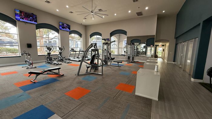 Spacious modern gym with high ceilings, exercise machines, and colorful carpeting.