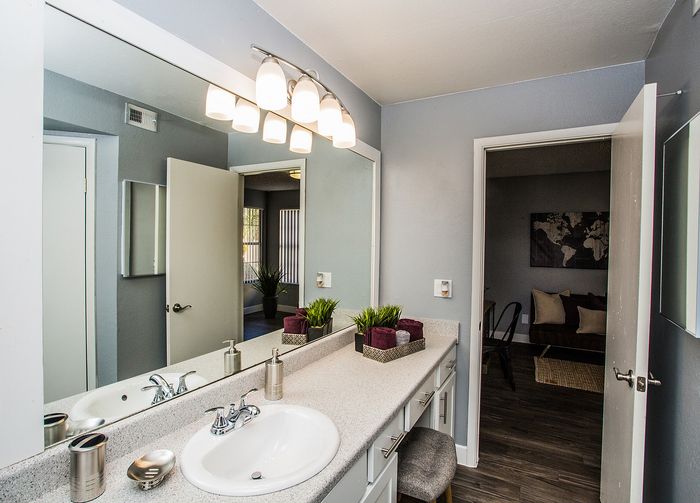 Chic bathroom with modern vanity, mirror lighting, and view into a cozy living room.