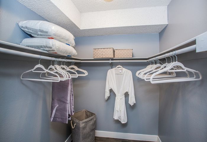 Elegant walk-in closet featuring ample hanging space with white hangers, storage bins, and pillows.