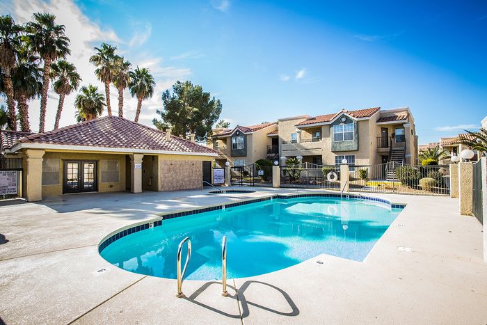 Charming apartment complex with a sparkling pool, palm trees, and sunny blue skies.