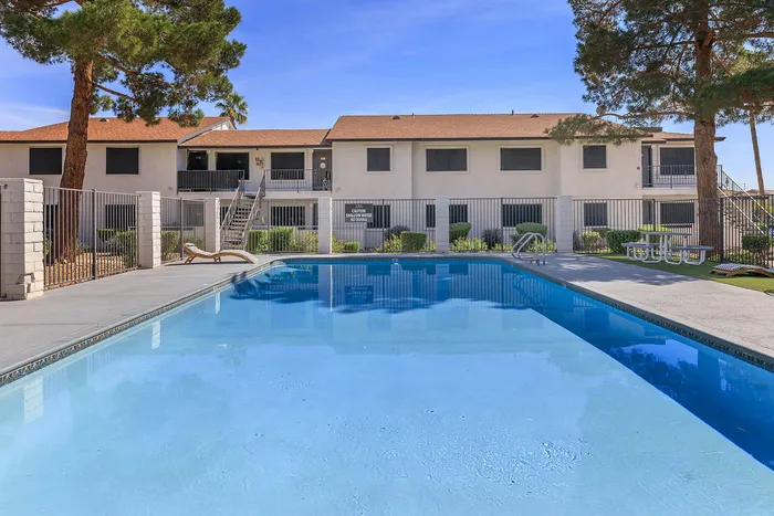 Bright and inviting apartment community pool with lounge chairs and surrounding greenery.