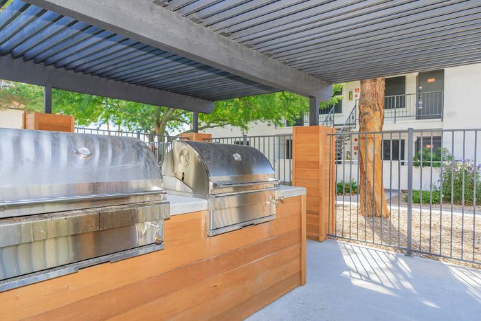 Elegant outdoor grilling station with stainless steel grills and wooden accents beneath a pergola.