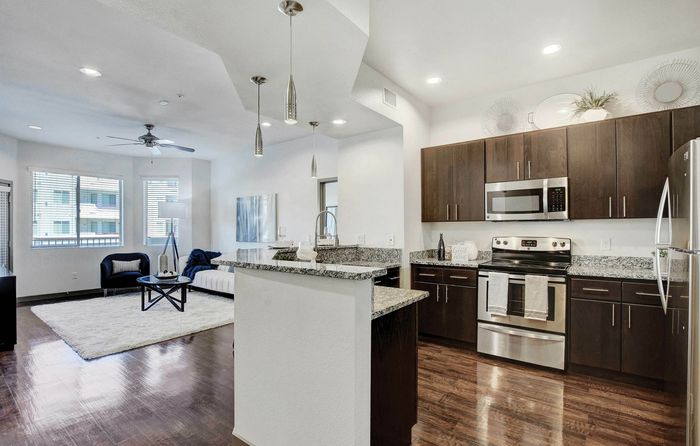 Modern open-concept kitchen and living area with sleek dark cabinets, stainless steel appliances, and elegant pendant lighting.