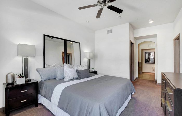 Modern bedroom with elegant decor, featuring a cozy king-size bed, stylish mirrored accents, and a chic ceiling fan for a luxurious ambiance.