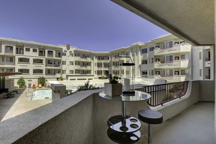 Charming apartment balcony with elegant seating overlooking a stylish community pool and contemporary apartment complex.