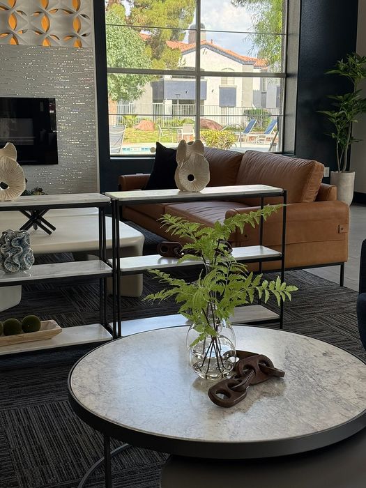 Elegant lounge area with modern decor, featuring a sleek leather sofa, artistic accents, and large windows overlooking a scenic pool area.