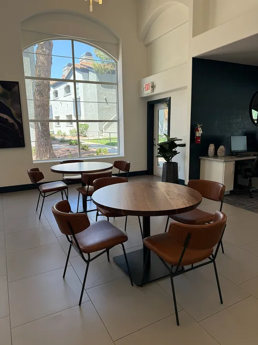 Chic communal space with modern round table, stylish leather chairs, and expansive arched window providing ample natural light.