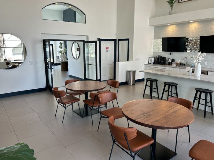 Chic, modern apartment lounge with stylish round tables, comfortable brown chairs, and a sleek bar area, perfect for social gatherings.