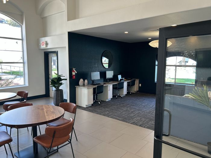 Modern and inviting apartment common area with sleek workstations, stylish round tables, and large windows for abundant natural light.