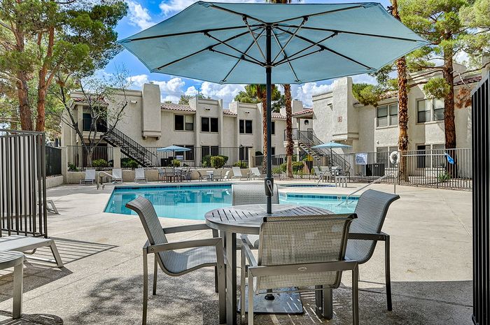 Charming apartment complex with a sparkling pool, inviting lounge chairs, and shade-providing umbrellas, perfect for relaxation.