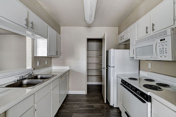 Bright and modern kitchen featuring sleek white cabinetry, stylish appliances, and rich wood flooring with an open pantry.