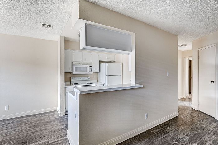 Charming apartment kitchen with white cabinets and modern appliances, featuring sleek wood flooring and open layout design.
