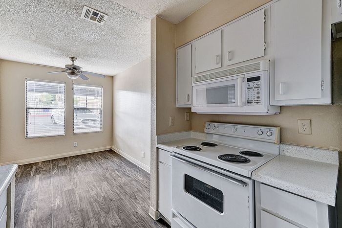 Bright kitchen with white cabinetry and spacious dining area featuring large windows and elegant wood flooring.