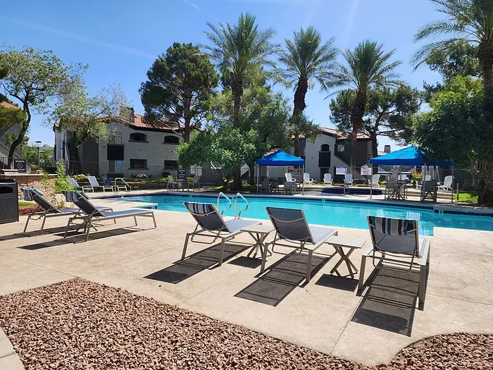 Inviting outdoor pool area with sun loungers, surrounded by lush palm trees and vibrant umbrellas, perfect for relaxation and leisure.
