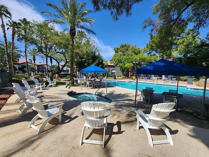 Luxurious apartment complex pool area featuring inviting lounge chairs, vibrant umbrellas, and lush greenery under a clear blue sky.