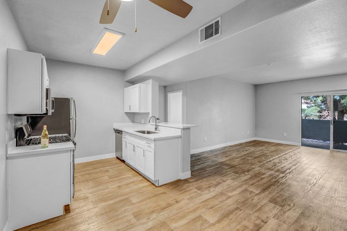 Bright, open-concept kitchen and living area with modern finishes, wood-style flooring, and a view of lush greenery through large patio doors.
