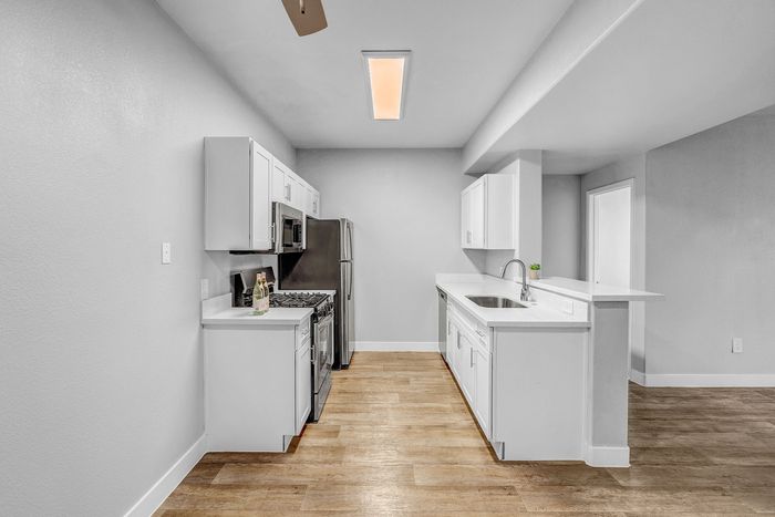 Modern kitchen with stainless steel appliances, sleek white cabinetry, and elegant wood flooring, perfect for contemporary living.