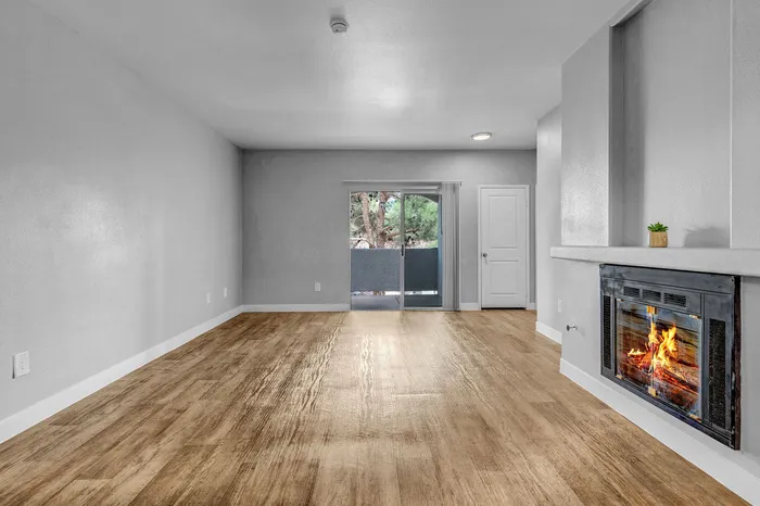 Modern living room with elegant hardwood floors, a cozy fireplace, and a view of greenery through glass doors.