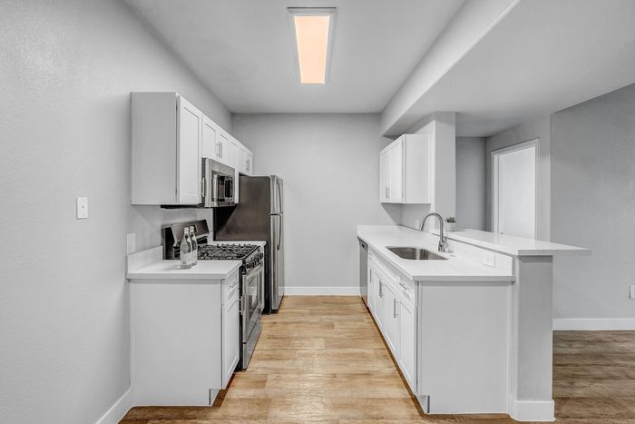 Modern kitchen with sleek white cabinetry, stainless steel appliances, and stylish wooden flooring for a contemporary feel.