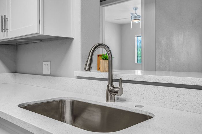 Modern kitchen with sleek stainless steel faucet, elegant white countertops, and a lush green plant by the window.