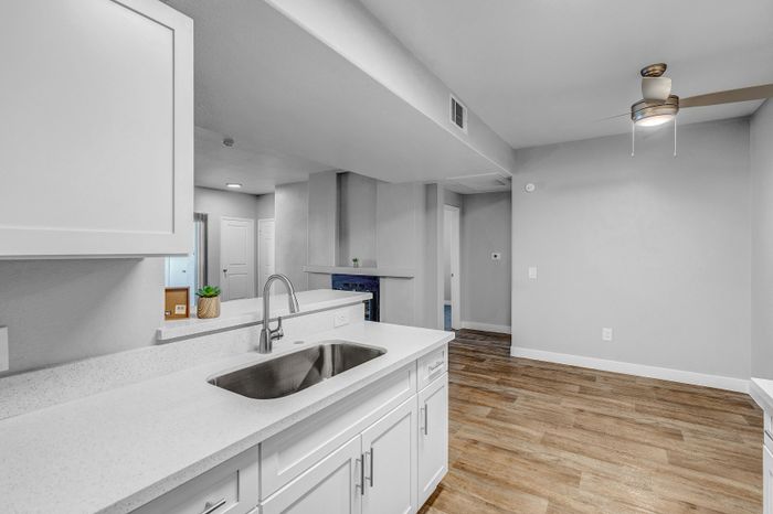 Modern kitchen with sleek white cabinetry and elegant countertops, featuring an open layout into a spacious living area with wood-style flooring and a contemporary ceiling fan.