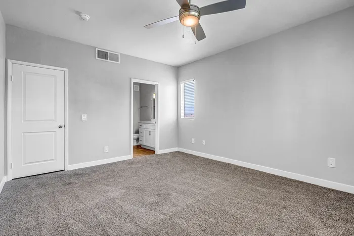 Bright and spacious bedroom with plush carpet, modern ceiling fan, and inviting ensuite bathroom.