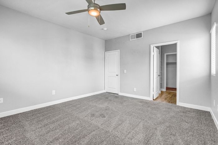 Bright and inviting bedroom with plush carpet and a modern ceiling fan, leading to a spacious walk-in closet.