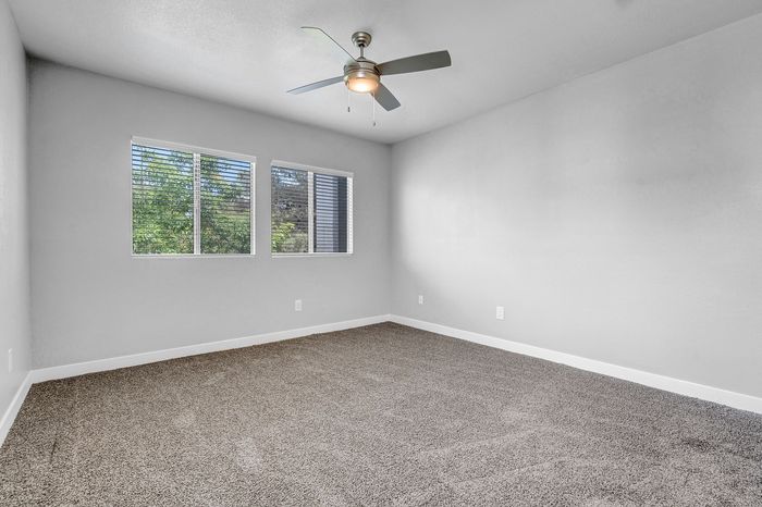 Bright and airy bedroom with a modern ceiling fan and large window overlooking lush greenery, featuring plush carpeting and neutral walls.