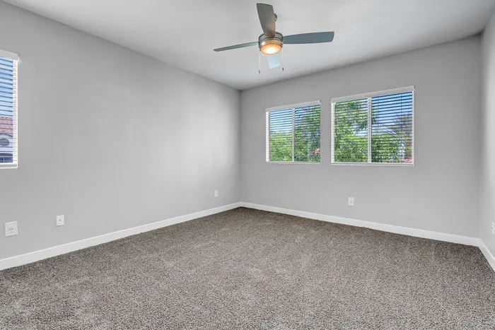 Bright and airy bedroom featuring a modern ceiling fan, plush carpeting, and large windows with scenic views.