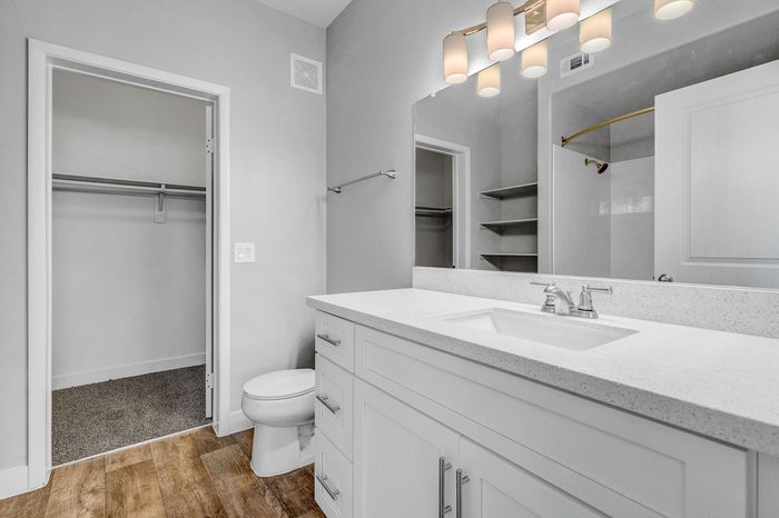 Modern bathroom with sleek white cabinetry, a large mirror, elegant lighting, and a spacious walk-in closet.