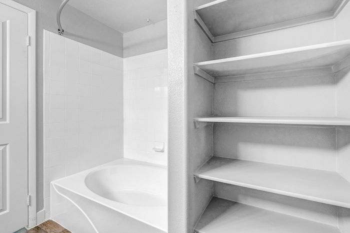 Modern bathroom with a sleek white bathtub and built-in shelving, perfect for organized storage.