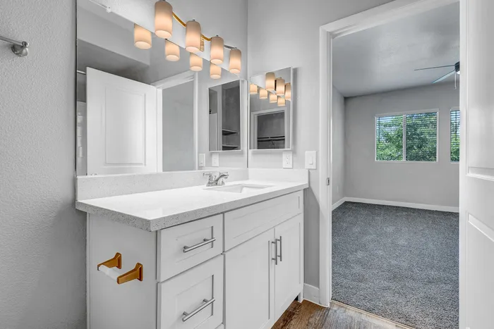 Elegantly designed bathroom with modern fixtures, bright vanity lighting, and an inviting view into a spacious bedroom.