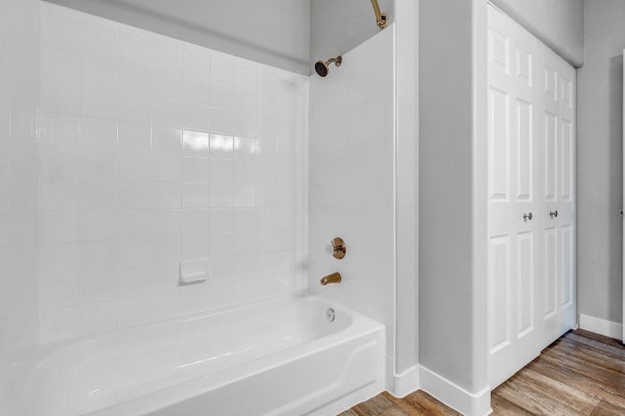 Bright modern bathroom featuring elegant white tiles, a sleek bathtub with brass fixtures, and stylish wood flooring.
