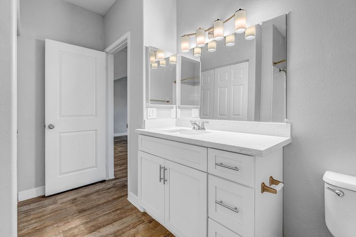 Modern bathroom with sleek white cabinet, elegant lighting, and warm wood flooring.