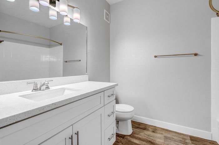 Bright, modern bathroom featuring sleek countertops, elegant lighting, and wood-style flooring.