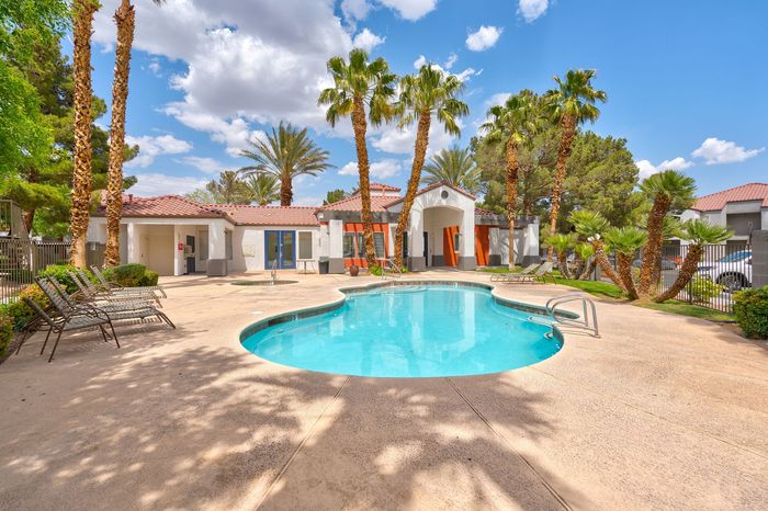 Inviting outdoor pool surrounded by palm trees and a stylish modern building, offering a perfect oasis for relaxation and leisure.