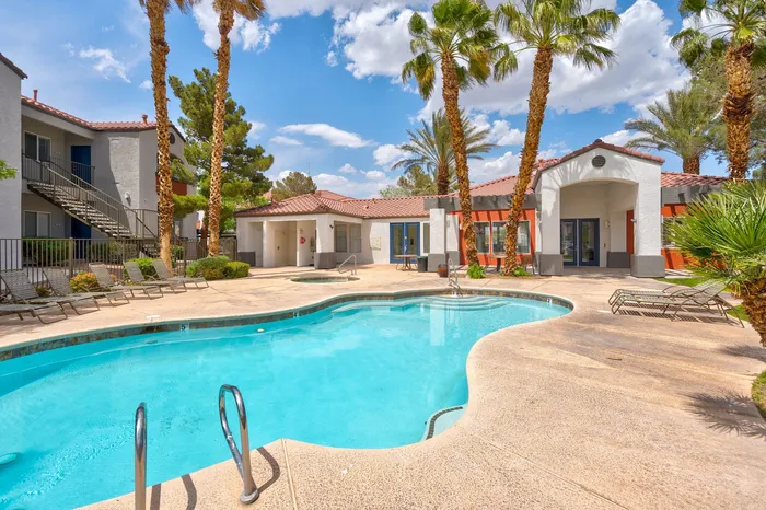 Inviting apartment complex pool area surrounded by palm trees and sun loungers, perfect for relaxing under the vibrant blue sky.