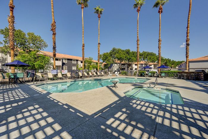Inviting community pool area with palm trees, lounge chairs, and a relaxing hot tub under a clear blue sky.