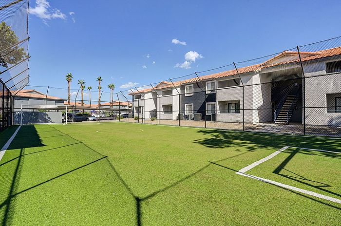 Inviting apartment complex featuring a sunlit sports field surrounded by lush greenery, perfect for active living.