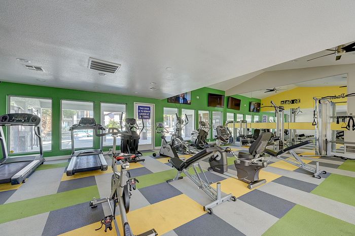 Bright and spacious fitness center with modern exercise equipment, vibrant green and yellow decor, and large windows overlooking the outdoor pool area.