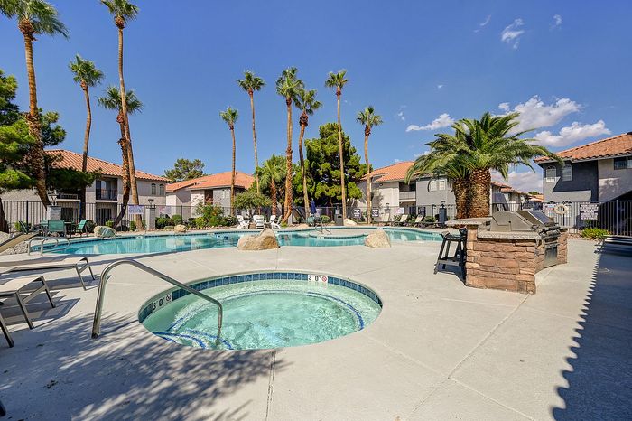 Inviting outdoor pool area with palm trees and a hot tub, surrounded by charming apartments and lush greenery.