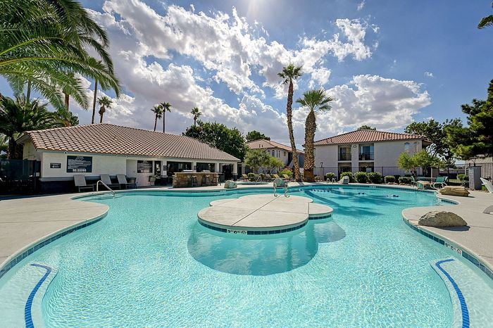 Luxurious resort-style swimming pool surrounded by palm trees, with modern outdoor seating and scenic views under a vibrant blue sky.
