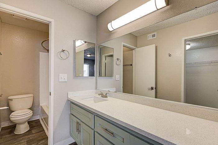 Bright and modern bathroom with a sleek countertop, large mirror, and elegant lighting, leading to a private shower area.