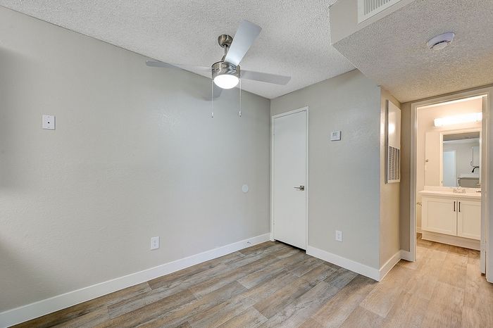 Modern room with sleek hardwood floors, a stylish ceiling fan, and a bright, inviting bathroom vanity area.