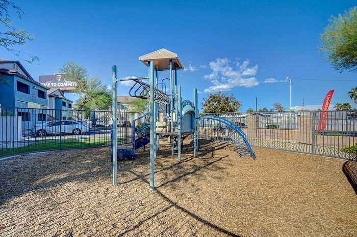 Inviting playground with blue climbing structures and slide, nestled in a sunny, fenced area ideal for family living.
