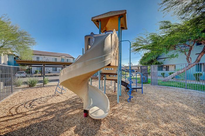 Charming playground with a spiral slide and climbing structures surrounded by a cozy, fenced area in a family-friendly apartment complex.