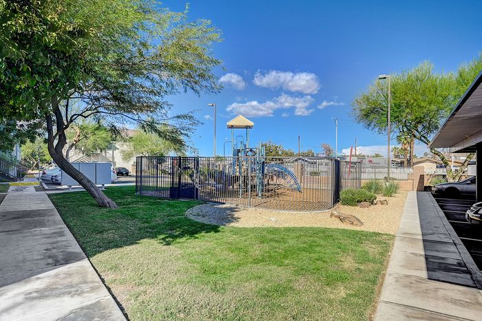 Inviting apartment complex with a vibrant play area, lush green lawn, and relaxing pathways under a bright blue sky.