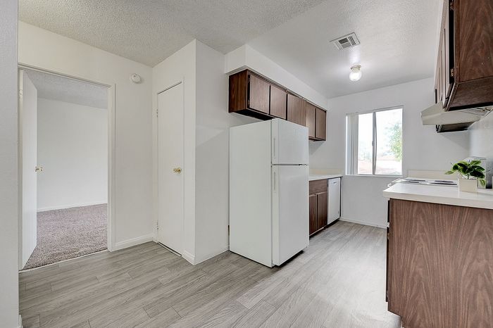 Bright and airy kitchen with modern appliances, wood cabinets, and elegant gray flooring, overlooking a cozy adjoining room.