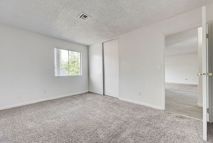 Bright and inviting room with plush carpeting, large window, and double sliding closet. Ideal space for a cozy bedroom or home office.