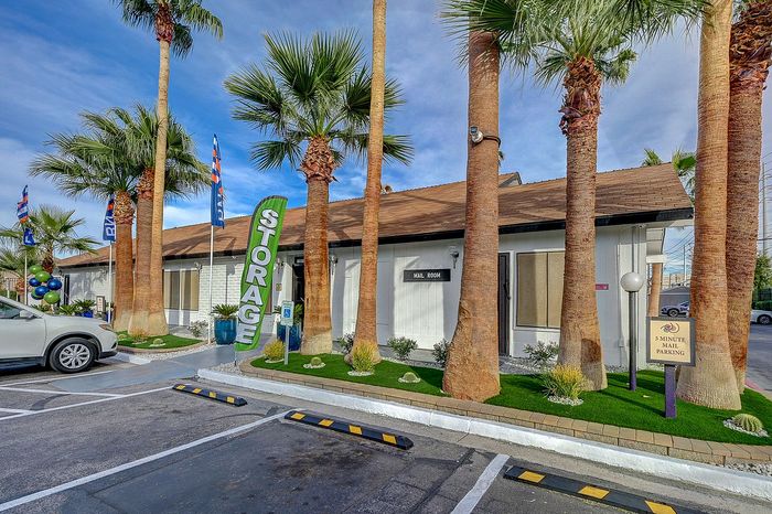 Inviting storage facility entrance surrounded by tall palm trees and ample parking.